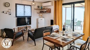 Ein modernes Wohnzimmer mit Essbereich, Fernseher, Kühlschrank und einem Fenster mit Vorhängen.
