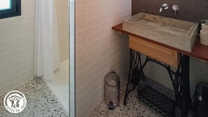 Ein Badezimmer mit Duschkabine aus Glas, rundem Spiegel, Holzwäscheschrank und Fliesenwand.
