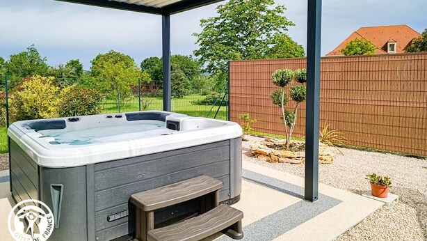 Ein Whirlpool unter einer  überdachten Terrasse mit einer Holzbank und einem kleinen Tisch.