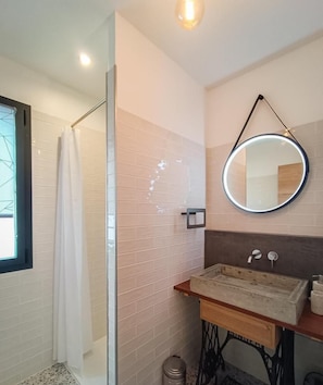 Une salle de bain avec une douche à parois de verre, un miroir rond, un meuble-lavabo en bois et un mur carrelé.