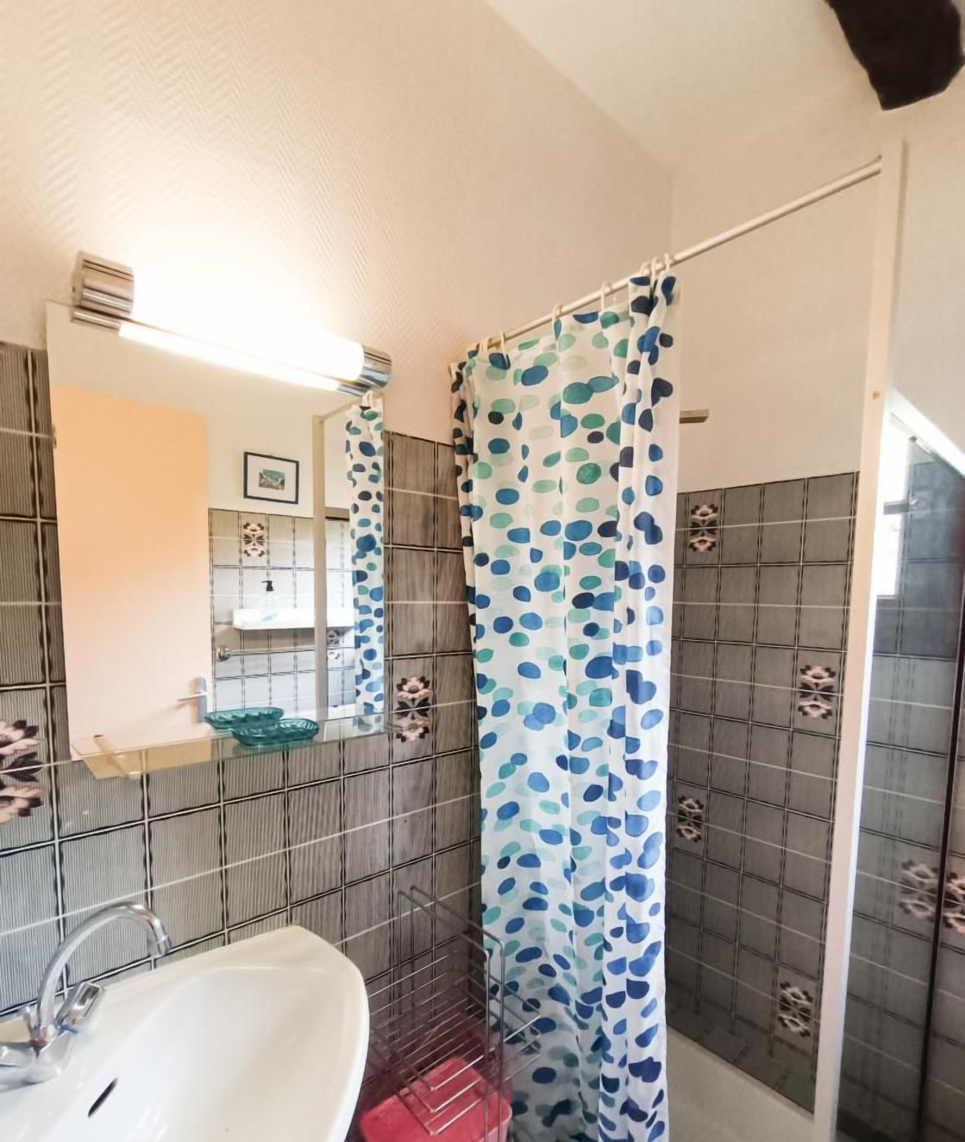 A bathroom with a white sink, a mirror, and a shower with a blue polka dot curtain.