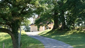 A gravel path leading to a stone building with a sloped roof, surrounded by lush greenery and trees.