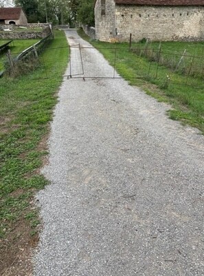 Un camino de grava que lleva a un edificio de piedra con una valla metálica a un lado.