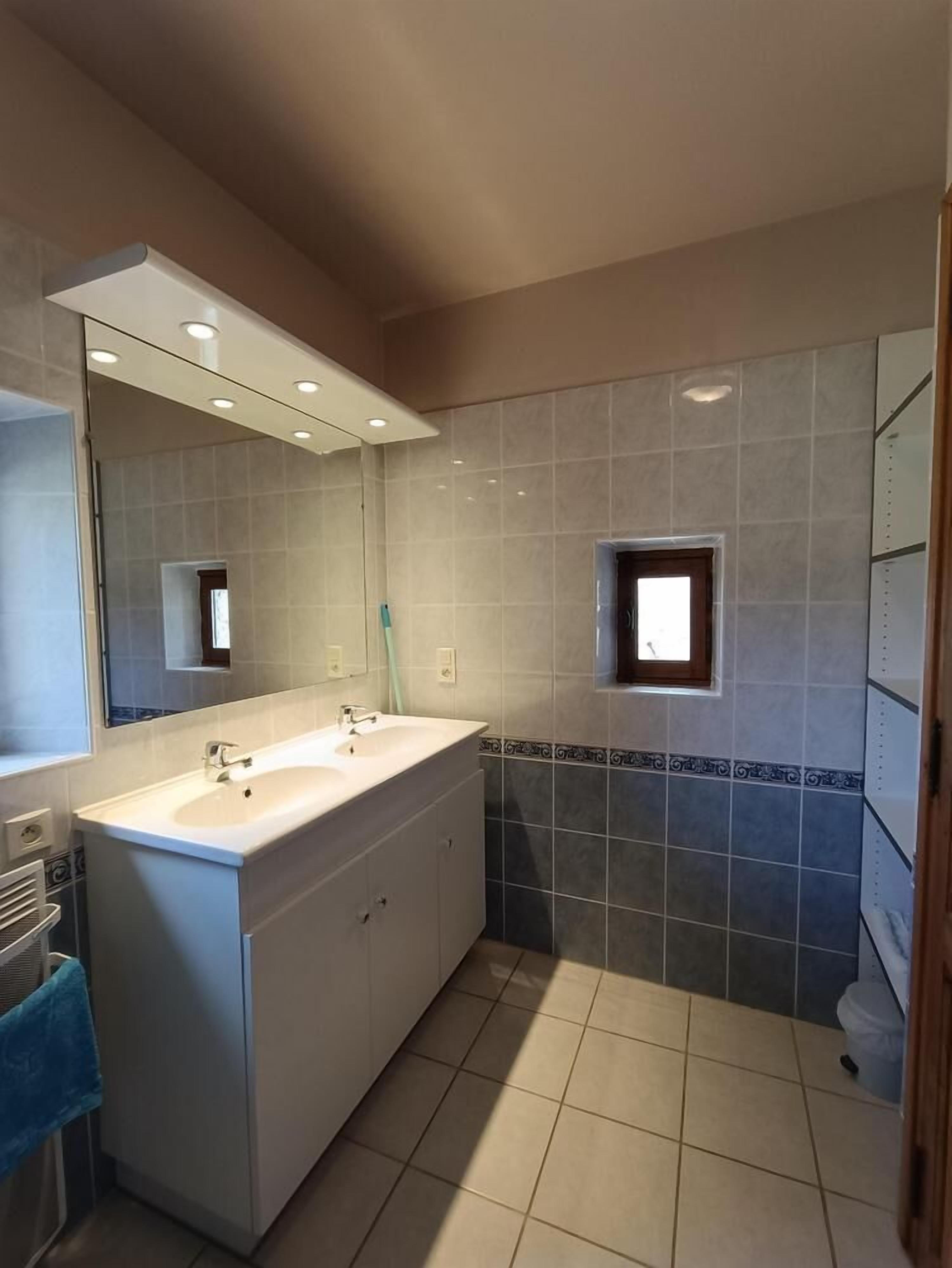 Une salle de bain moderne avec deux lavabos, un grand miroir et une petite fenêtre.
