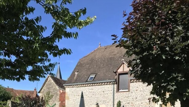 Een stenen huis met een tuin, met rode en witte bloemen, een gazon en een stenen rand.