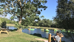 Een park aan het meer met picknicktafels, een houten terras en opblaasbaar water speelgoed.