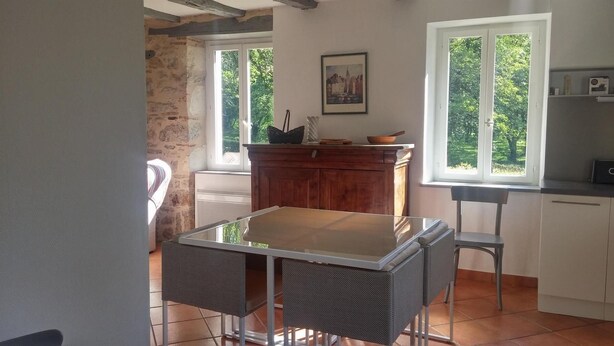 A dining area with a glass-top table and wicker chairs, a wooden cabinet, and a view through a window. - Gîtes de France® - LE MOULIN (CREYSSE)