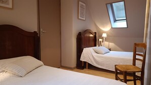 A bedroom with two beds, a wooden wardrobe, a small table with a lamp, and a window with a view. - Gîtes de France® - LE MOULIN (CREYSSE)