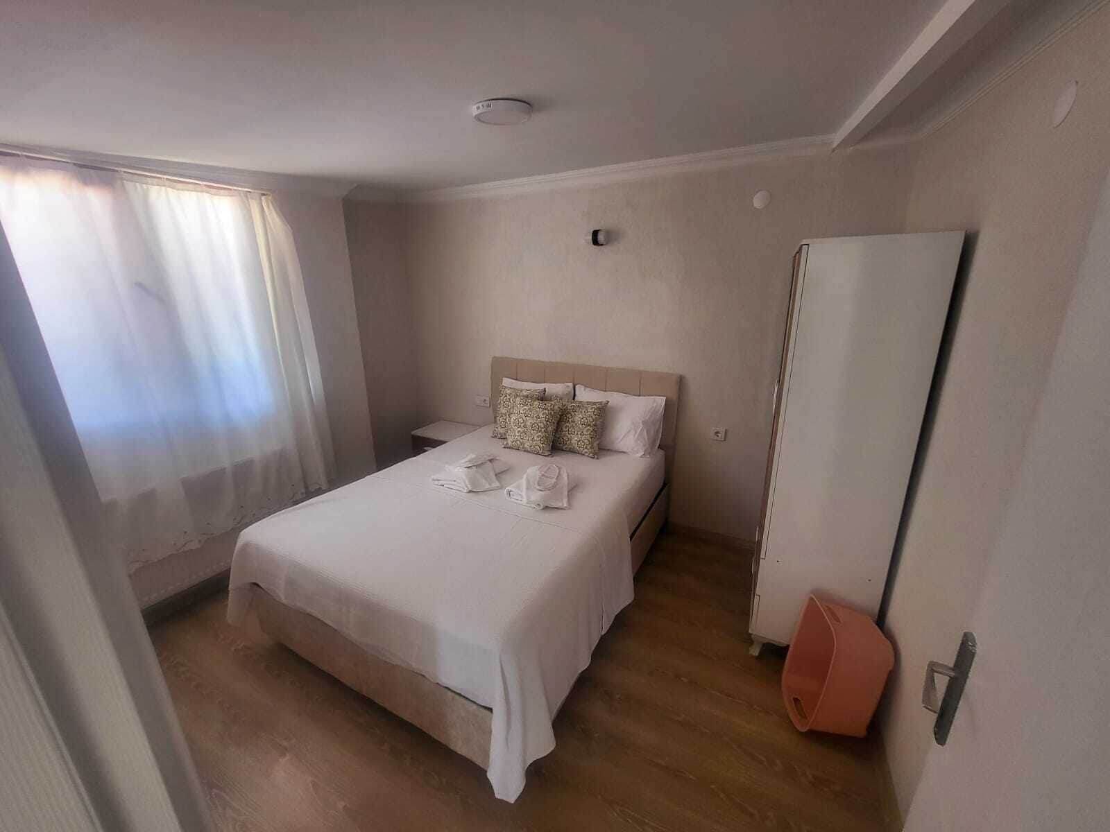 Una habitación de hotel con cama, mesita de noche, armario y ventana con cortinas.