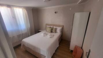 Una habitación de hotel con cama, mesita de noche, armario y ventana con cortinas.