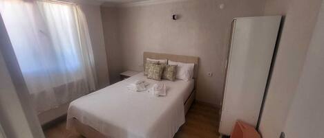 Una habitación de hotel con cama, mesita de noche, armario y ventana con cortinas.