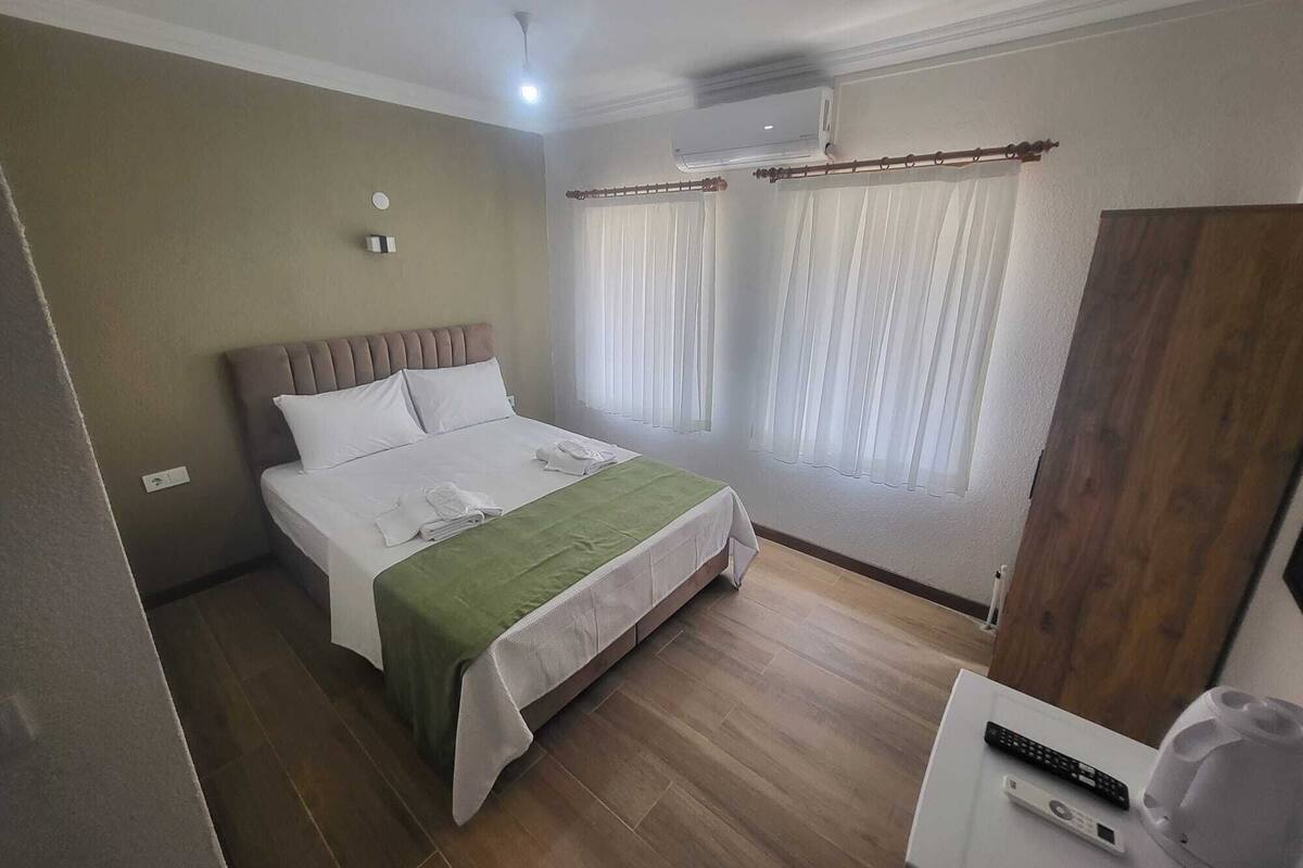 A hotel room with a bed, a desk, a chair, a TV, and a window with curtains.