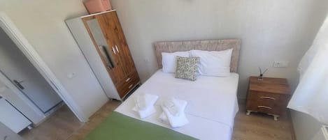 Un dormitorio ordenado con una cama, un armario de madera, una mesita de noche pequeña y una colcha verde.