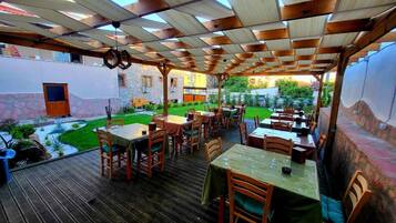 Un restaurante al aire libre con mesas y sillas de madera, una terraza de madera y un jardín.