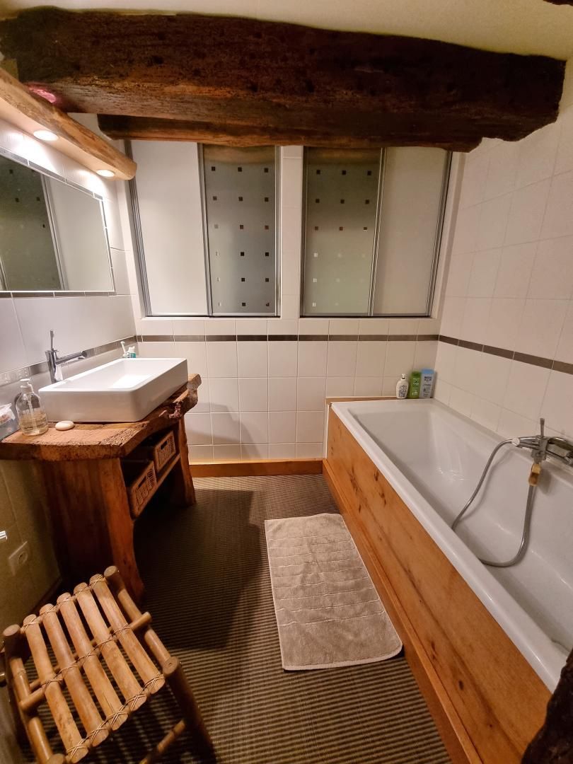 Un baño con tocador de madera, una bañera grande y un ventanal con vidrio esmerilado.