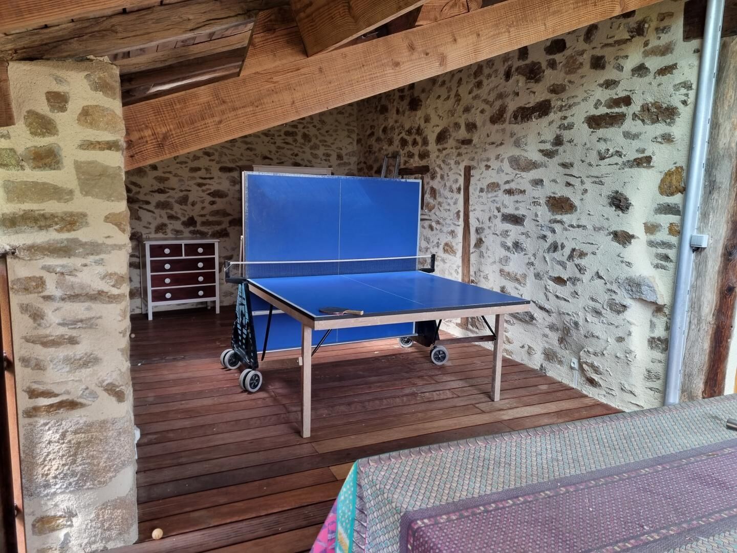 Uma mesa de pingue-pongue num quarto rústico com paredes de pedra, chão de madeira e um pequeno baú.