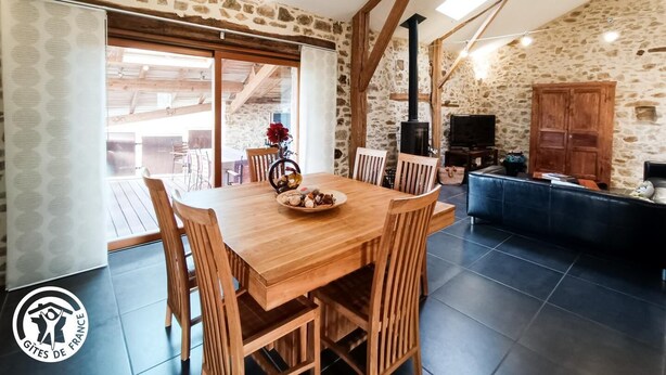 A rustic interior with a wooden dining table, stone walls, and a stone fireplace. - Gîtes de France® - Gîte de Larigaldie (SAINT CIRGUES)