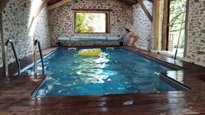 An indoor swimming pool with stone walls, wooden beams, and a bench. - Gîtes de France® - Gîte de Larigaldie (SAINT CIRGUES)