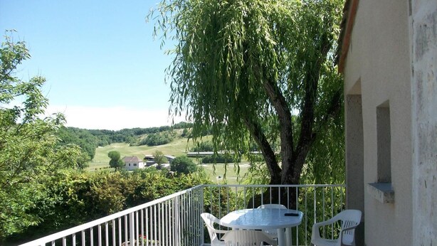 A balcony with a table and chairs, overlooking a green landscape with trees and a distant house. - Gîte de Sisamé - Pern (PERN)