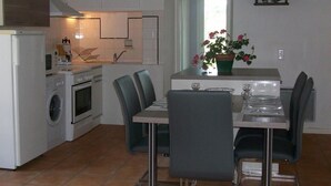 A compact kitchen with a washing machine, oven, and microwave. There is a dining area with a table set for two and a potted plant on the window sill. - Gîte de Sisamé - Pern (PERN)