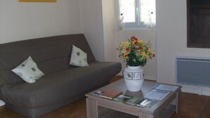 A living room with a grey sofa, a white vase with flowers, and a small table with magazines. - Gîte de Sisamé - Pern (PERN)