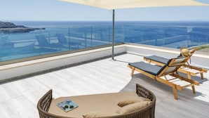En balkon med gelænder af glas, en træloungestol, en fletstol og et magasin på gulvet.