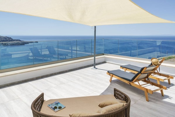 A balcony with a glass balustrade, a wooden lounge chair, a wicker chair, and a magazine on the floor.