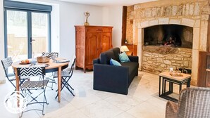 A living room with a stone fireplace, a dining area with a table and chairs, and a large window. - Domaine de Ratier - LES Arques (LES ARQUES)