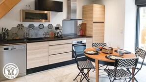 A modern kitchen with a dishwasher, microwave, and wooden cabinets. There is a dining area with a round table and chairs. - Domaine de Ratier - LES Arques (LES ARQUES)