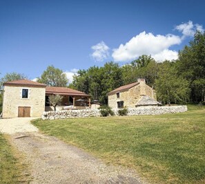 A stone house with a red-tiled roof, a gravel driveway, and a grassy lawn.