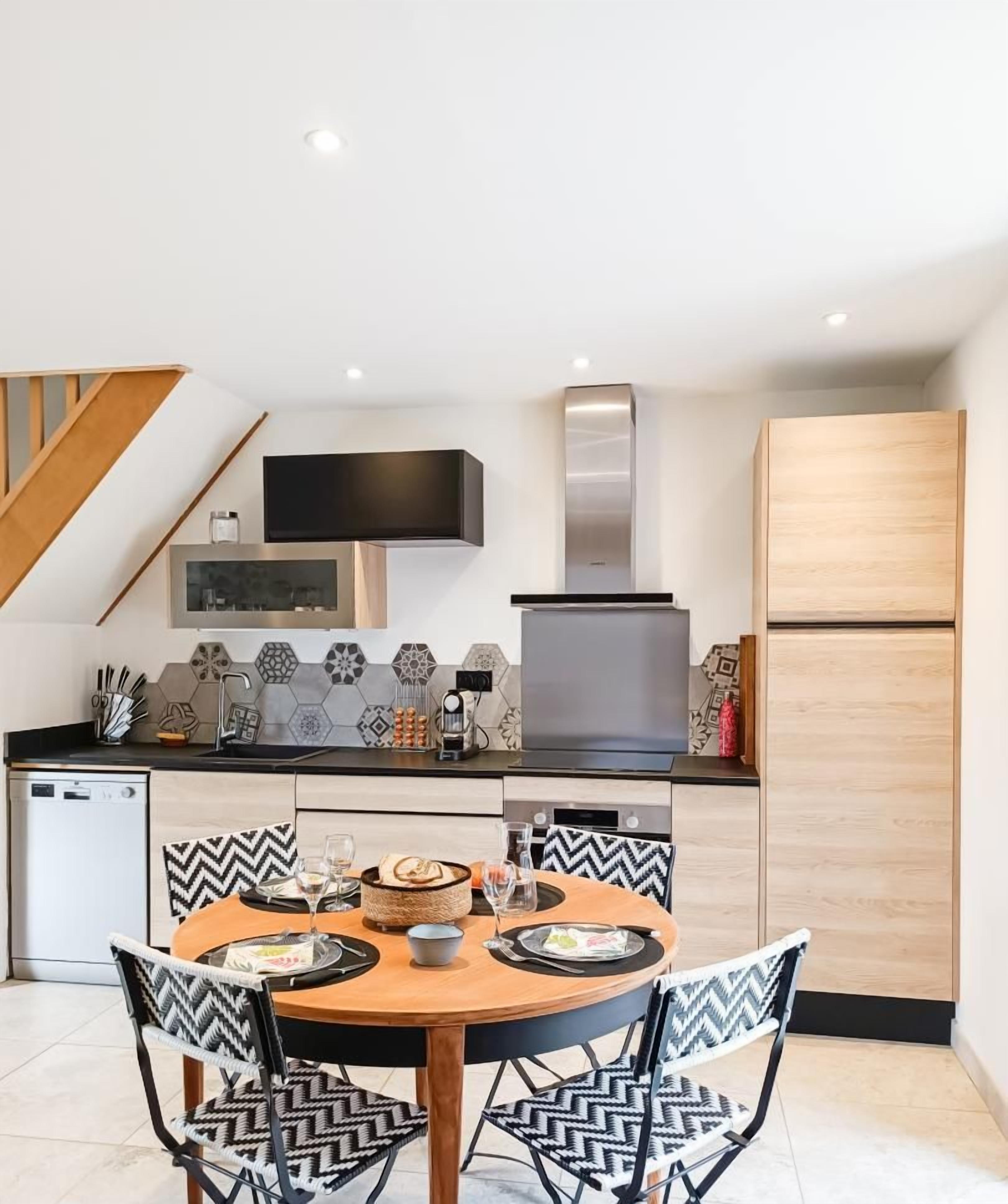 Una cocina moderna con comedor, que incluye una mesa redonda, sillas con estampado blanco y negro, horno empotrado y refrigerador de acero inoxidable.