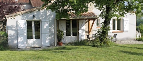 A white building with a tiled roof, a covered porch, and a small garden area with a table and chairs.