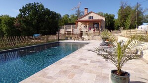 Uma piscina com deck de pedra, cerca de madeira e uma casa ao fundo.