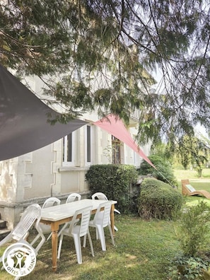 An outdoor dining area with a table and chairs, a large umbrella, and a building in the background. - Gîtes de France® - Gary's Mill (SAINT-LAURENT-LES-TOURS)