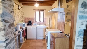 Una cocina rústica con paredes de piedra, vigas de madera, piso de baldosas, una estufa, un fregadero y un reloj.
