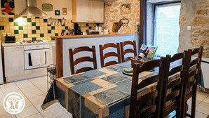 Una cocina con pared de piedra, una mesa de comedor de madera y una lámpara colgante.