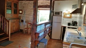 A rustic kitchen with wooden cabinets, a refrigerator, and a microwave. - Gîtes de France® - Le Fournil (SOULOMES)