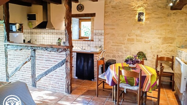 A rustic kitchen with a stone wall, wooden beams, and a tiled backsplash. - Gîtes de France® - Le Fournil (SOULOMES)