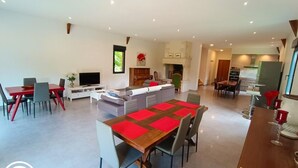 A spacious living area with a dining table, sofas, and a kitchen in the background. - Gîtes de France® - Le Hangar (MEYRONNE)