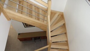A wooden staircase with metal handrails, leading to a room with a tiled floor and a black sign with white letters. - Gîtes de France® - Le Hangar (MEYRONNE)