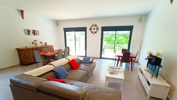 A modern living room with a sectional sofa, a dining area, and a TV on a stand. - Gîtes de France® - Le Hangar (MEYRONNE)