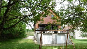 A rustic barn with a swing set in a lush green garden. - Gîtes de France® - Le Hangar (MEYRONNE)