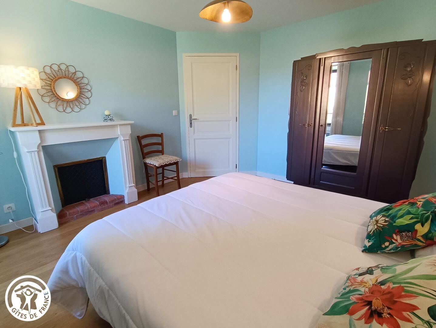A bedroom with a bed, a chair, a wardrobe, a mirror, and a fireplace.