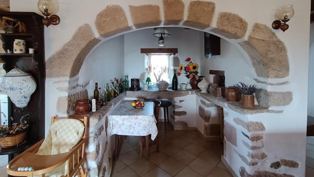A rustic kitchen with stone walls, a wooden ceiling, and a dining area with a table set for two.