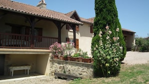 A traditional building with a tiled roof, a balcony with wooden railings, and a stone wall with potted plants.