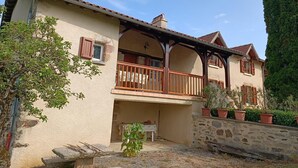 A two-story house with a balcony, stone walls, and potted plants.