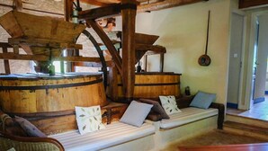 A rustic interior with a wooden barrel, a bench with cushions, wicker furniture, and a wooden table.