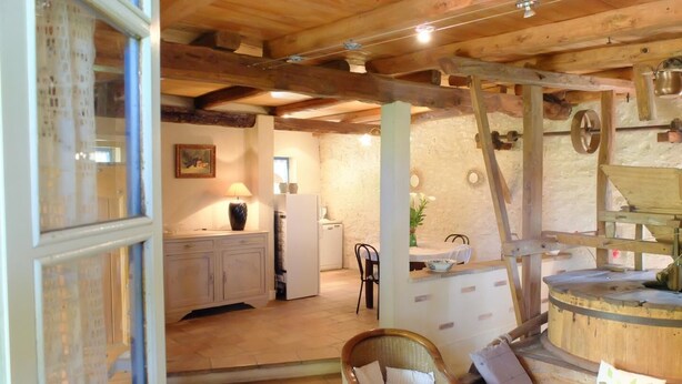 A rustic interior with a wooden ceiling, a dining area, a kitchen, and a seating area with a bench and cushions.