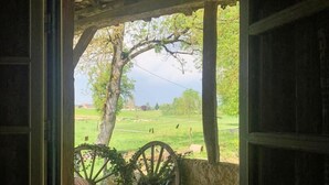 A rustic wooden porch with a bench and a wheelbarrow, overlooking a green landscape.