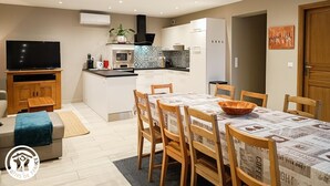 Una cocina moderna con armarios blancos, un microondas y una cafetera. Hay una mesa de comedor con sillas y un televisor sobre un mueble.